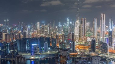 Dubai 'nin panoramik silueti, iş sahası ve şehir merkezi gece zaman çizelgesi. Birçok modern gökdelenin havadan görünüşü. Kanalda tekneler. Birleşik Arap Emirlikleri.