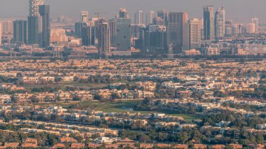 Jumeirah Village Circle 'ın zaman çizelgesinin hava görüntüsü, Dubai' de bir radyal topluluk. Gün batımında turuncu akşam ışığında gökdelenler ve villalar