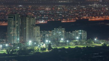 Dubai marinasından yeşilliklerin hava görüntüsü gece saat dilimi. Yukarıdan caddelerde trafik olan kuleler ve gökdelenler. Arka planda ve golf sahasında villalar