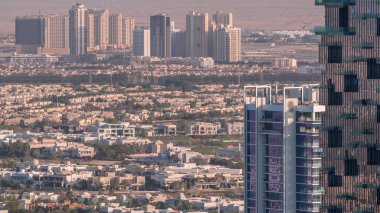 Jumeirah Village Circle 'ın zaman çizelgesinin hava görüntüsü, Dubai' de bir radyal topluluk. JLT 'nin gökdelenleri ve turuncu akşam ışığında birçok villa