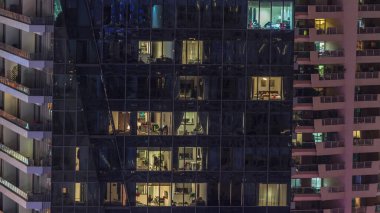 Modern ofisteki pencere ışıkları ve geceleri konut binaları. Çok katlı gökdelenlerin içinde aydınlık odalar ve cam yüzeyden yansımalar var.