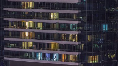 Geceleri modern binalardaki pencere ışıkları zaman ayarlı. İçinde aydınlık odalar olan çok katlı gökdelenler.
