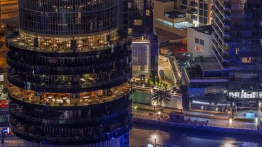 Dubai marinası rıhtımı ve her katta farklı restoranlar olan binalar gece gündüz geçiş zamanları. Nehir, rıhtımı ve gökdelenleri olan yatlar güneş doğmadan önce.