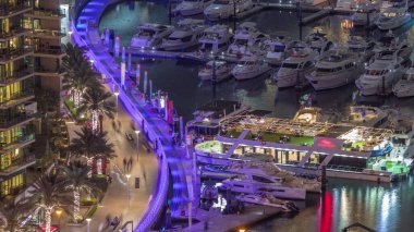 Kanal çevresindeki Dubai marina rıhtımına gece vakti yüzen yatların görüntüsü. Yat kulübünde beyaz tekneler var.