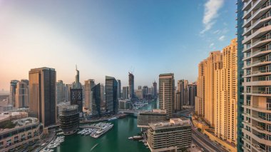 Kanal etrafındaki Dubai marina gökdelenlerinin hava panoramik görüntüsü gün doğumunda yüzen teknelerle birlikte. Yat kulübünde beyaz tekneler var.