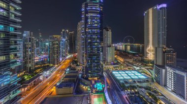 Dubai Marina ve JBR bölgesinin panoramik manzarası ve ünlü dönme dolap gece zaman çizelgesi ve aydınlatılmış gökdelenler.