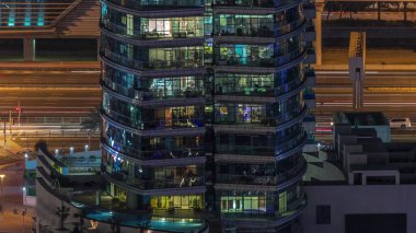 Gece vakitlerinde apartmanların pencereleri, evlerin pencerelerinden gelen ışık. Parlak odalı şehrin akşam manzarası. Gökdelenin arkasındaki trafik