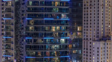 Gece vakitlerinde apartmanların pencereleri, evlerin pencerelerinden gelen ışık. Parlak kuleleri olan şehrin akşam manzarası