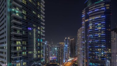 Dubai Marina ve JBR bölgesinin panoramik manzarası ve aydınlık gökdelenlerle dolu gece hava trafiği. Arkaplanda koyu yıldızlı bir gökyüzü