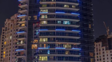 Gece vakitlerinde apartmanların pencereleri, balkonlu evlerin pencerelerinin ışığı. Parlak odalı şehrin akşam manzarası