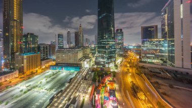 Dubai Uluslararası Finans Bölgesi gece gündüz geçiş zamanı. Gün doğmadan önce iş yerinin panoramik hava görüntüsü. Oteller ve otoparklarla aydınlatılmış gökdelenler.