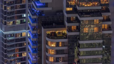 Modern kulelerin pencerelerinde ışık var. Geceleri parlayan pencereleri ve balkonları olan bir apartmanın dışında. Gökdelenin yukarıdan aydınlatmalı havadan görünüşü