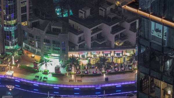 Dubai Marina 'daki hava manzaralı gezinti alanı palmiyeler ve yatlar ile aydınlatıldı. Rıhtımdaki yürüme alanı boyunca restoranlar. Dubai, Birleşik Arap Emirlikleri