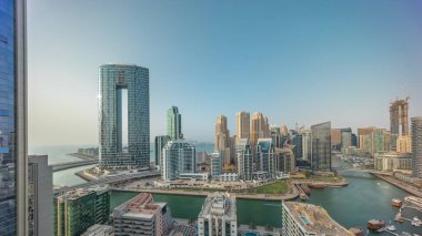 Dubai Marina gökdelenleri ve lüks binaları ve tatil köylerinin zaman çizelgeleri olan JBR bölge panoraması. Palmiyeler ve kanalda yüzen teknelerle dolu bir liman.
