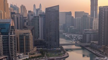 Dubai Marina 'da limanda tekneleri ve yatları var. Gün doğumunda kanalın etrafında gökdelenler var. Ilık ışıklarla dolu kuleler.
