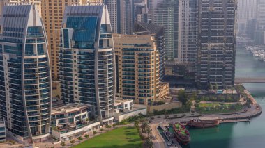 Güneş doğarken Dubai Marina gökdelenleri ve JBR bölgesi lüks binaların ve tatil yerlerinin uzun gölgeleriyle dolu. Palmiyeler ve kanalda yüzen ahşap botlarla dolu bir liman.