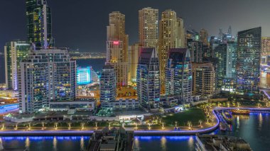 Dubai Marina 'da rıhtımın yakınına park edilmiş birkaç tekne ve kanal havası etrafında aydınlık gökdelenler var. Arka planda JBR bölgesi kuleleri