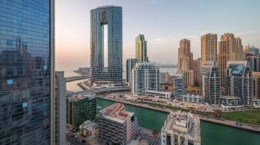 Günbatımından sonra Dubai Marina gökdelenleri ve JBR semti aydınlanmış lüks binalar ve gece geçiş zamanlarıyla dolu tatil köyleri. Palmiyeler ve kanalda yüzen teknelerle dolu bir liman.
