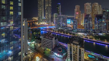 Dubai Marina gökdelenleri ve lüks binaları olan JBR semti ve yollarda trafiği olan gece uçuşları. Aydınlatılmış rıhtım ve kanalda yüzen tekneler