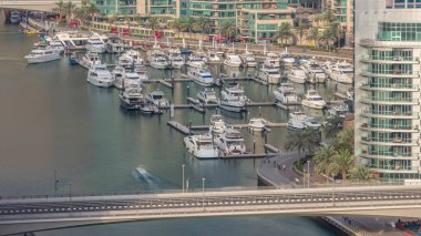Birçok yat ve tekne liman havası zaman dilimine park edilmiştir. Dubai Marina rıhtımı yürüyüş alanı. Modern tekne derede yüzüyor. Köprüde trafik