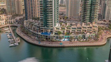 Dubai Marina Havaalanı 'nda palmiyeler ve birçok kafeyle rıhtım gezintisi. Yatlar ve tekneler suda yüzüyor.