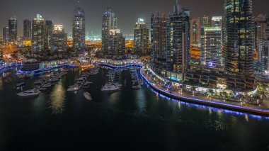 Dubai marinasındaki havadan gece saatlerinde lüks yat körfezi panoraması. Rıhtım boyunca modern gökdelenler ve limanda yüzen tekneler.