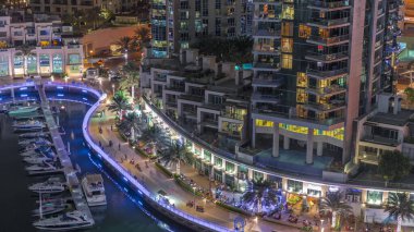 Dubai Marina Havacılık Gecesi 'nde palmiyelerle ve birçok restoranla rıhtımda gezinti. Yatlar ve tekneler rıhtımın yakınında yüzüyor.