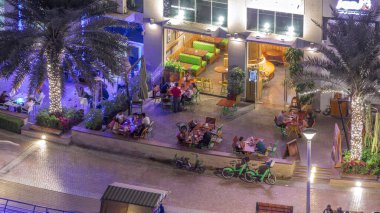 Açık teras, masaları ve sandalyeleri olan restoran manzaralı gece manzaralı bir yer. Dubai marinası yakınlarında birlikte yemek yiyen insanlar.