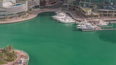 Dubai Marina 'da avuçiçi avuçlarla rıhtım gezintisi. Yatlar ve tekneler suyun üzerinde yüzüyor. Yeşil suyu olan kanal.