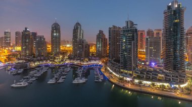 Gündoğumundan önce Dubai marinasında gece gündüz lüks yat hangarında geçiş zamanı. Rıhtım boyunca modern gökdelenler ve limanda yüzen tekneler.
