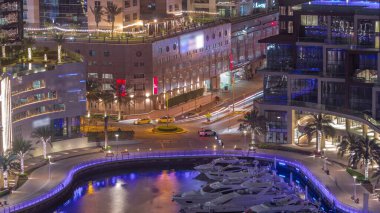 Dubai Marina hava sahasında palmiyelerle rıhtım gezintisi. Yatlar ve tekneler suyun üzerinde yüzüyor. Yolda trafik vardı.