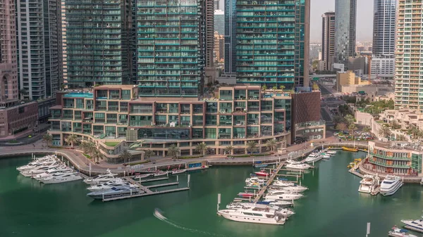 Dubai Marina 'da avuçiçi avuçlarla rıhtım gezintisi. Yatlar ve kayıklar suyun üzerinde yüzer ve arka planda yüksek gökdelenler