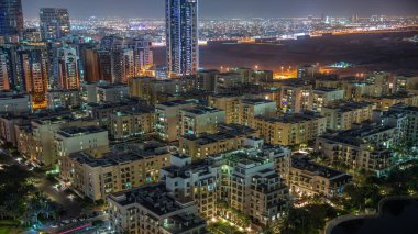 Yeşiller bölgesindeki alçak katlı binalar ve Barsha Heights bölgesindeki gökdelenler gece uçuşları. Aydınlatılmış binalarla Dubai silueti