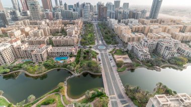 Barsha Heights bölgesindeki gökdelenler ve Greenens bölgesindeki alçak binalar. Dubai ufuk çizgisi aşağı bak. Palmiyeler ve ağaçlar göle yakın.