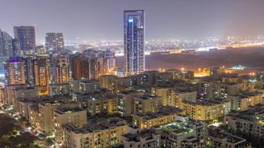 Barsha Heights bölgesinde gökdelenler ve tüm gece boyunca Greenens bölgesinde alçak binalar. Dubai silueti arkaplanda çöl var.