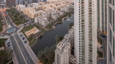 Yeşiller bölgesindeki havuz ve alçak katlı binalar gündüz ve gece geçiş zamanları. Arka planda Barsha Heights bölgesinde gökdelenleri olan Dubai gökdelenleri