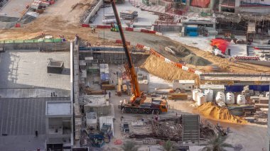 Vinçler ve buldozerler yeni gökdelen hava zaman çizelgesinin şantiyesinde çalışıyorlar. Arazi temizliği, not verme, havuz kazma, siper kazma ve temel kazma. Sürüngen traktörü ve yer değiştirme ekipmanları