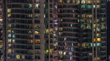 Apartman binasının parlayan pencerelerinin gece görüşü. Yüksek gökdelende odalar ve balkon ışıkları var.