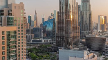 Dubai şehir merkezi. Gün doğumu sırasında hava saatinin etrafında en yüksek gökdelenler var. Güneş ışınları ve yansımaları kulelerin cam yüzeyinden