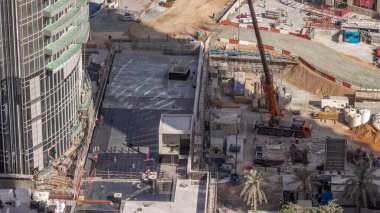 Vinçler ve buldozerler yeni gökdelen hava zaman çizelgesinin şantiyesinde çalışıyorlar. Çatı kaplaması. Arazi temizliği, not verme, havuz kazma, siper kazma ve temel kazma. Sürüngen traktörü ve yer değiştirme ekipmanları