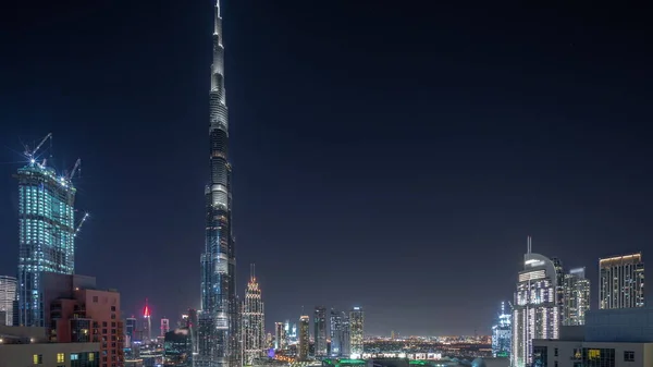 Dubai Downtown panoramic cityscape with tallest skyscrapers around aerial during all night timelapse. Construction site of new towers from above and lights turning off