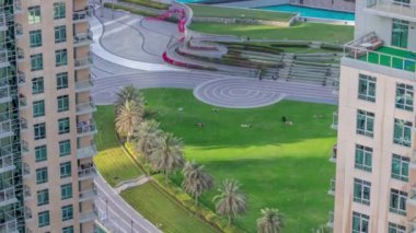 Fıskiyelerin yanındaki yeşil çimenli park. Dubai şehir merkezindeki yapay göl çevresindeki kuleler.