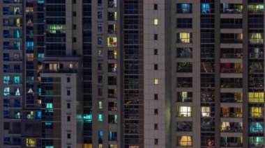 Gece karanlığında parlayan gökdelen dairesinin pencereleri şehrin ışıklarını yansıtıyor..