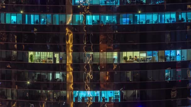 Gece karanlığında parıldayan parlak gökdelenin ofis pencereleri şehrin ışıklarını yansıtıyor.. — Stok video