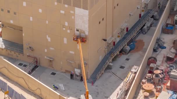 Travailleurs de la construction dans le seau de véhicule de grue pour la restauration et la réparation de la façade du bâtiment timelapse aérienne. — Video
