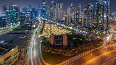 Business Bay havacılık panoramik gece zaman çizelgesinde aydınlatmalı modern kuleleri olan Bay Avenue, Dubai, BAE. Büyük otoparkın yakınındaki yolda trafiği olan gökdelenler.
