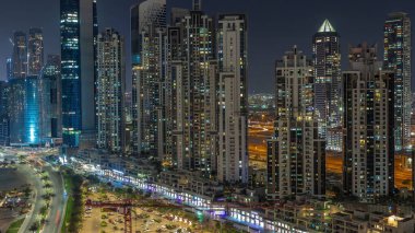 Business Bay hava sahasında modern kuleleri olan Bay Bulvarı. Gece uçuşu, Dubai, BAE. Parlak pencereli gökdelenler