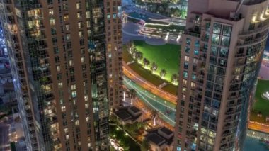 Fıskiyelerin yanındaki yeşil çimenli park. Dubai şehir merkezindeki yapay göl çevresindeki kuleler.