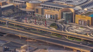 Dubai şehir merkezinde, alışveriş merkezinin girişine yakın otoban trafiği ve birçok taksisi var. Gökdelen çatısı, otopark ve otobüs durağı manzaralı.