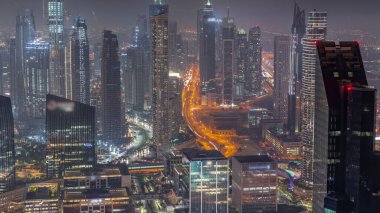 Şehir merkezinin ufuk çizgisi, modern mimari biçimle gece zamanının üstünde. Dubai iş hangarı kulelerinin hava görüntüsü. Gökdelenler arasındaki yollarda trafik